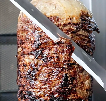 Beef doner being carved from the spit with a long knife